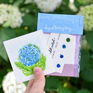 以下が含まれることがあります： 白いカードに青いアジサイの花の水彩画。カードは、青3色と緑1色を含むアジサイのミニペイントキットの一部です。