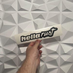 May include: White sticker with black text that reads "hella rust" in a stylized font.