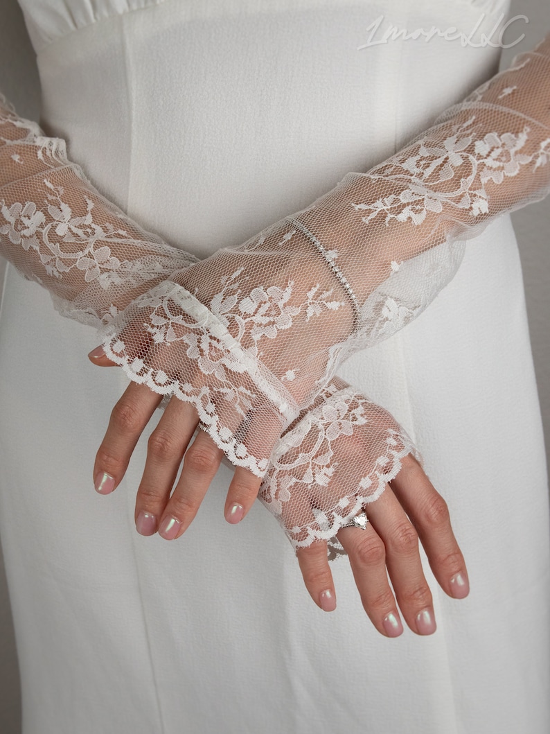May include: A pair of white lace gloves with a delicate floral pattern. The gloves are sheer and have a scalloped edge.