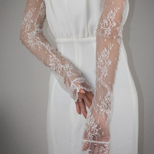 May include: A pair of white lace gloves with a floral pattern. The gloves are long and reach to the elbows. The gloves are made of a delicate, sheer fabric.