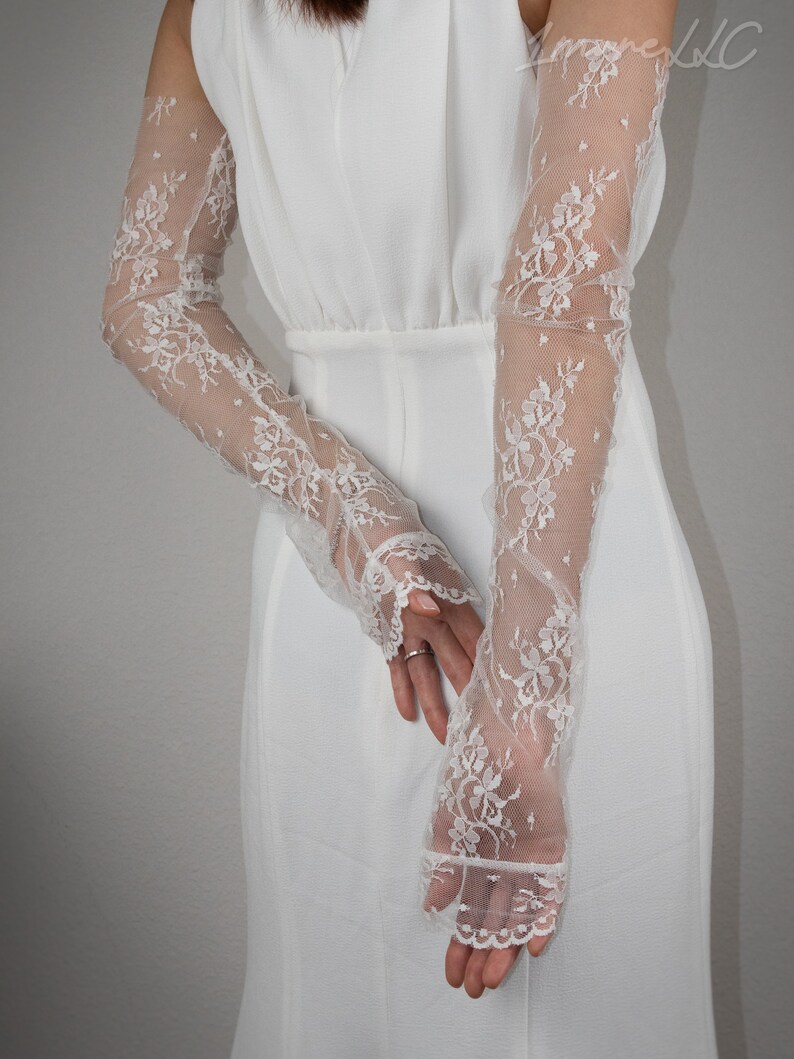 May include: A pair of white lace gloves with a floral pattern. The gloves are long and reach to the elbows. The gloves are made of a delicate, sheer fabric.
