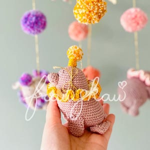 Puede incluir: M&oacute;vil de beb&eacute; hecho a mano de ganchillo con un elefante rosa con cuello y sombrero amarillos y naranjas. El m&oacute;vil incluye pompones y banderines de fieltro de colores en tonos rosas, amarillos y morados, suspendidos de un aro dorado.
