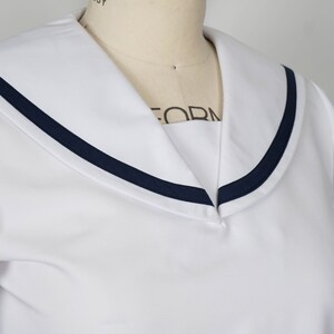 Cropped shot showcasing the details of a white seifuku top with a navy blue trimmed sailor collar and short sleeves with matching navy blue trim. The top is displayed on a mannequin.