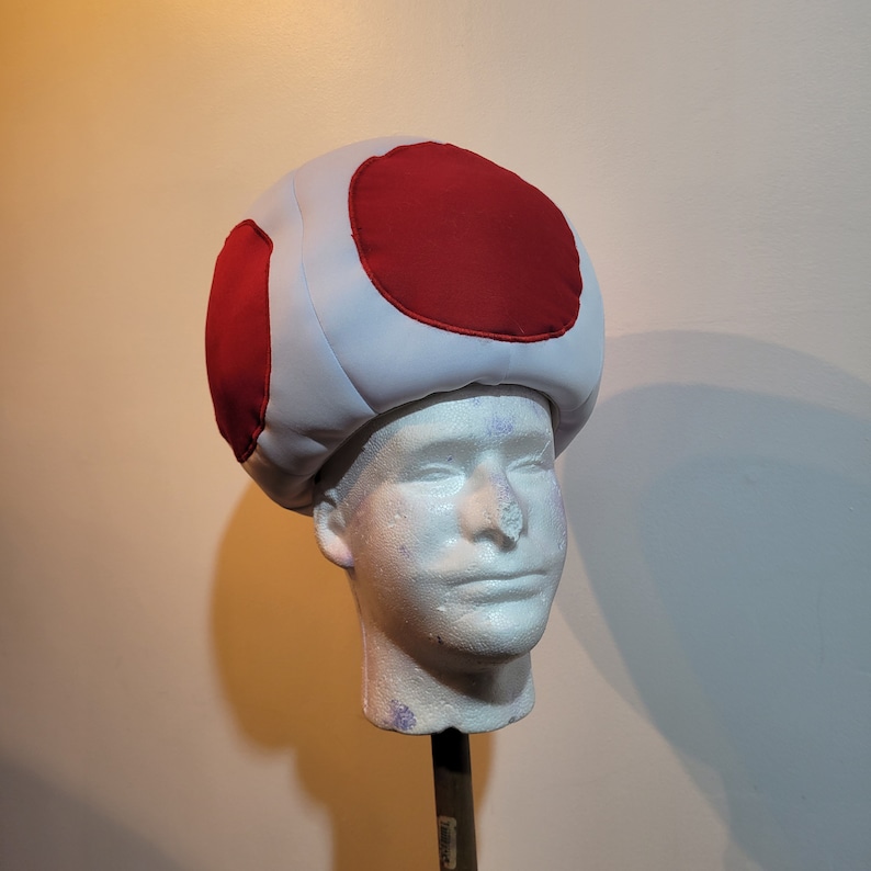 Photo of mushroom hat that ressembles a sphere with 4 big red dots, in the front, back and sides of the hat. The hat fit snuggly on the head.