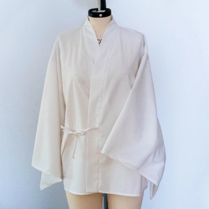 Puede incluir: Una chaqueta blanca de estilo kimono con mangas largas y un cintur&oacute;n de lazo. La chaqueta est&aacute; hecha de una tela ligera y tiene un dise&ntilde;o simple y elegante.