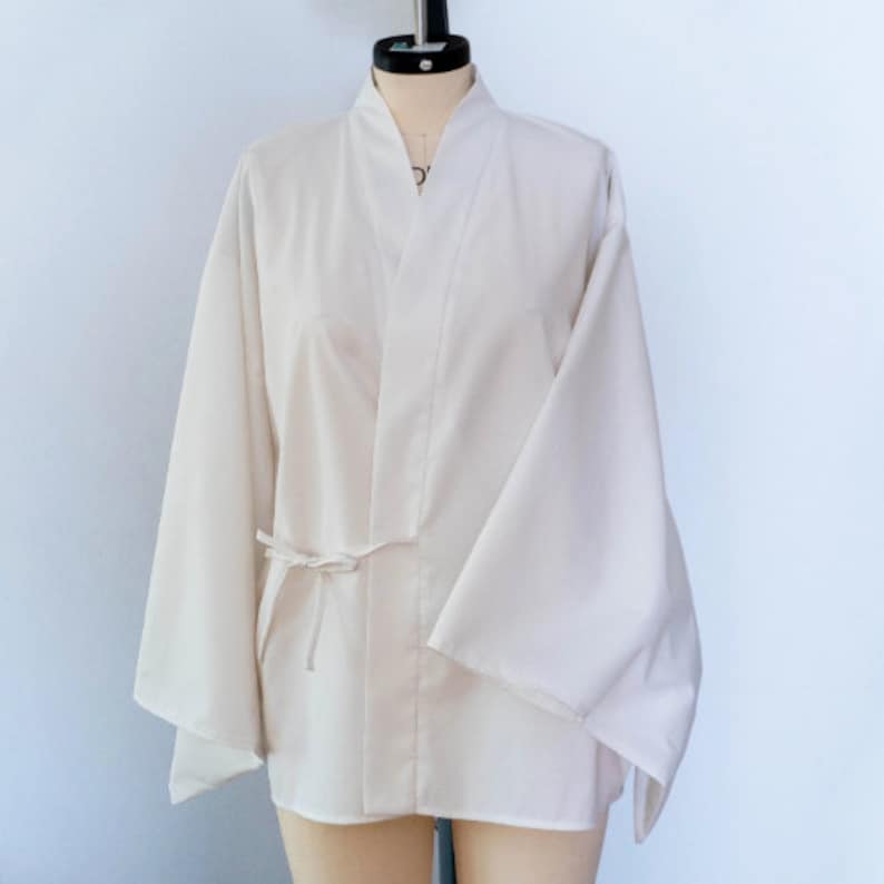 Puede incluir: Una chaqueta blanca de estilo kimono con mangas largas y un cintur&oacute;n de lazo. La chaqueta est&aacute; hecha de una tela ligera y tiene un dise&ntilde;o simple y elegante.