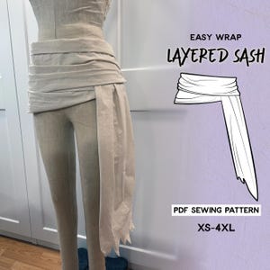 Peut inclure: Un châle superposé beige clair, présenté sur un mannequin. Le châle est enroulé autour de la taille et tombe sur le côté. L'image comprend le texte "EASY WRAP LAYERED SASH" et "PDF SEWING PATTERN XS-4XL".