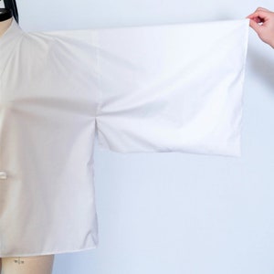Puede incluir: Un kimono blanco con mangas largas. Las mangas est&aacute;n dobladas hacia atr&aacute;s y sostenidas por una mano.