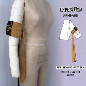 May include: A tan and black arm band with gold detailing is wrapped around a mannequin arm. The arm band features the number "37" in gold. The text "EXPEDITION ARMBAND" and "PDF SEWING PATTERN" are visible. Bicep size is 29cm - 42cm.