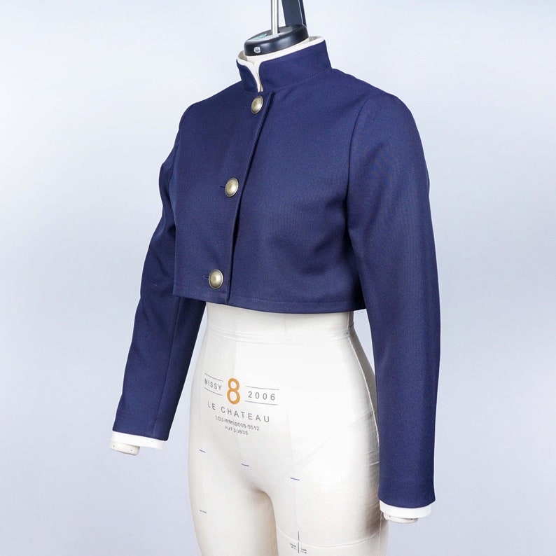 May include: A navy blue cropped jacket with gold buttons and a white collar. The jacket is on a white dress form.