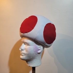 Photo of mushroom hat that ressembles a sphere with 4 big red dots, in the front, back and sides of the hat. The hat fit snuggly on the head.