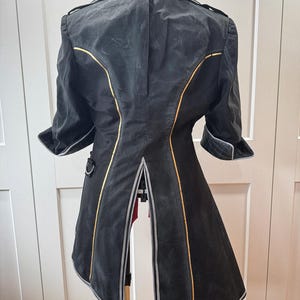 May include: A black coat with gold and silver trim, displayed on a dress form. The coat features a notched collar, short sleeves, and a split back. The design includes decorative stitching and a tailored fit.