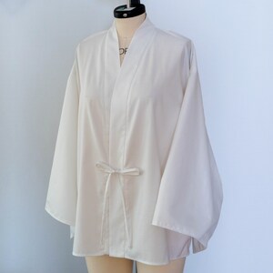 Puede incluir: Un kimono blanco con cierre de lazo. El kimono tiene mangas largas y un corte holgado.