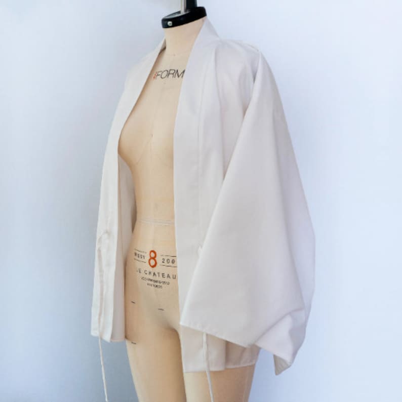 Puede incluir: Una chaqueta blanca de estilo kimono con mangas largas y cierre de nudo. La chaqueta est&aacute; hecha de una tela ligera y tiene un dise&ntilde;o simple y elegante.