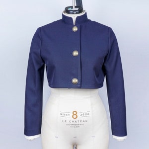 May include: A navy blue cropped jacket with gold buttons and a mandarin collar. The jacket is on a white dress form. The label on the dress form reads "Missy 8 2006 LE CHATEAU LCU-WMS0008-0612 AVF 30835"