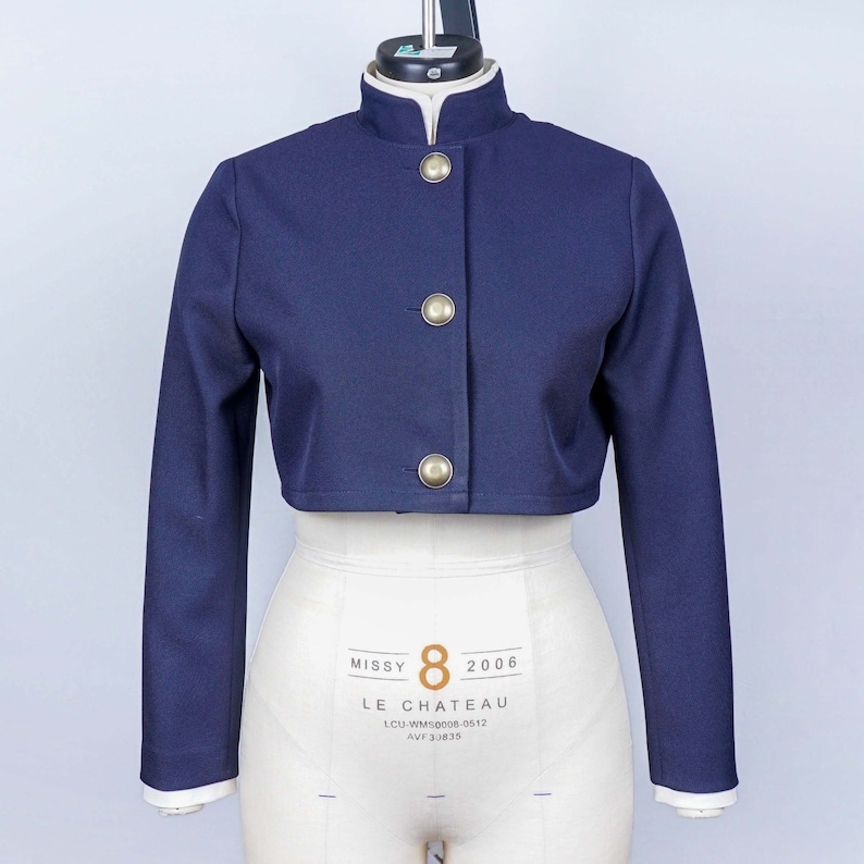May include: A navy blue cropped jacket with gold buttons and a mandarin collar. The jacket is on a white dress form. The label on the dress form reads "Missy 8 2006 LE CHATEAU LCU-WMS0008-0612 AVF 30835"