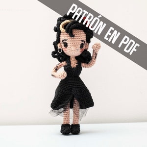 Peut inclure: Poupée crochetée avec des cheveux noirs et une robe noire. La poupée a des tatouages sur les bras et porte des chaussures noires. Le texte "PATRÓN EN PDF" est dans le coin supérieur droit.