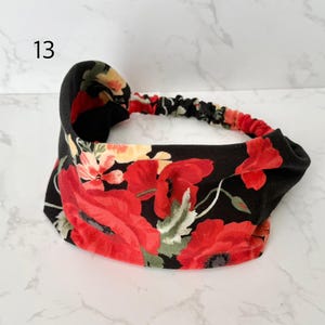 May include: A fabric headband featuring a black background with a vibrant floral pattern of large red poppies, smaller yellow flowers, and green leaves. The accessory includes a gathered elastic band section at the back for a secure fit.