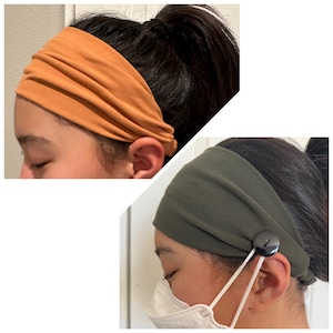 May include: Two wide fabric headbands, one in a solid burnt orange color and the other in a solid olive green color. The olive green headband features a black button on the side, designed to hold the elastic loops of a white face mask in place.