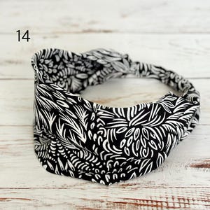 May include: A black and white headband featuring a repeating abstract botanical pattern with a twisted knot detail at the top. The number 14 is printed in the upper left corner of the image. The fabric has a wide, gathered design.