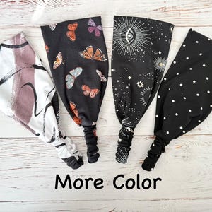May include: Four fabric headbands with elastic back bands. The first is white with black and mauve brushstrokes. The second is black with orange and purple butterflies. The third is black with white celestial sun and star motifs. The fourth is black with white polka dots. Text reads: More Color.