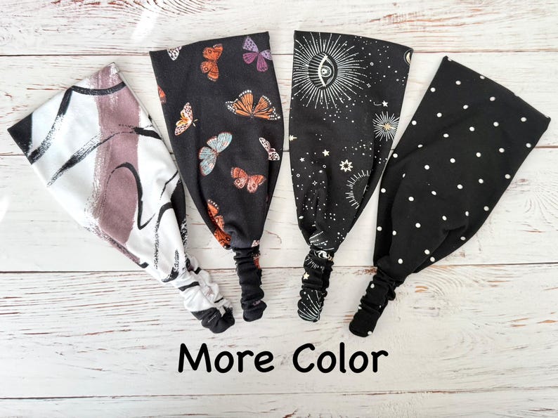 May include: Four fabric headbands with elastic back bands. The first is white with black and mauve brushstrokes. The second is black with orange and purple butterflies. The third is black with white celestial sun and star motifs. The fourth is black with white polka dots. Text reads: More Color.