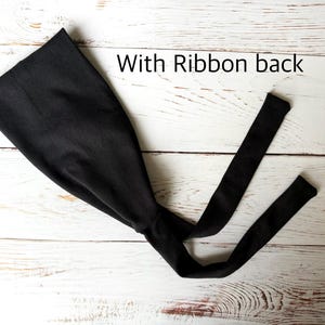 May include: A solid black headband featuring a wide front section that tapers into two long, thin fabric ties at the back. The text "With Ribbon back" is printed in black letters above the headband, which is displayed flat.