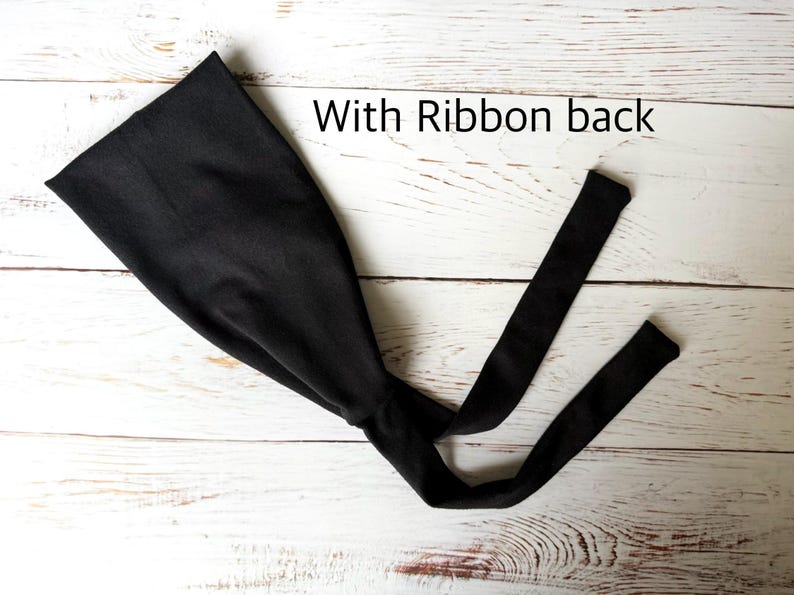 May include: A solid black headband featuring a wide front section that tapers into two long, thin fabric ties at the back. The text "With Ribbon back" is printed in black letters above the headband, which is displayed flat.