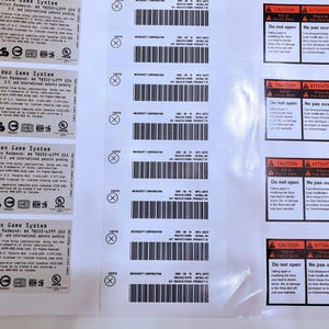 Könnte beinhalten: Eine Sammlung weißer Etiketten mit schwarzem Text und Barcodes. Die Etiketten sind für ein Xbox Video Game System, mit Warnhinweisen und Herstellerinformationen. Die Etiketten sind rechteckig und glänzend.