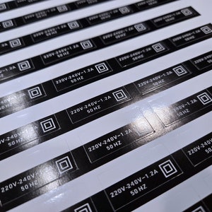 May include: Close-up of multiple black and white labels with the text "220V-240V-1.2A 50 HZ" printed on them.