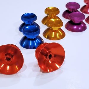 Op de afbeelding: Assortiment van kleurrijke vervangende duimstokken voor videogamecontrollers. De duimstokken zijn gemaakt van metaal en zijn verkrijgbaar in rood, oranje, blauw en paars.