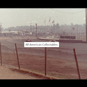 May include: Vintage photograph of a car race. Two race cars are on the track, with spectators in the background. The image has a sepia tone, and the text "All American Collectables" is visible.