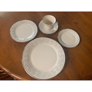 Könnte beinhalten: Ein Set weißer Geschirrteile mit silbernem Rand und einem zarten Blumenmuster. Das Set enthält einen Speiseteller, einen Salatteller, eine Untertasse und eine Teetasse.