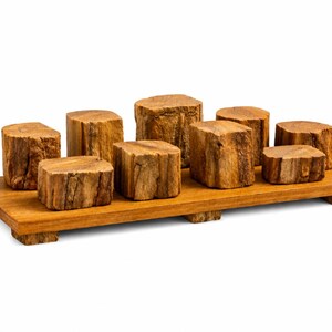 Könnte beinhalten: Ein rechteckiges Holztablett mit vier kleinen Füßen, auf dem acht zylindrische Holzblöcke unterschiedlicher Höhe stehen. Das Tablett und die Blöcke weisen eine natürliche hellbraune Holzmaserung mit organischen Mustern auf.