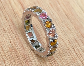 May include: A silver band ring with a row of colorful gemstones. The gemstones are set in a silver band and are arranged in a circle around the ring.