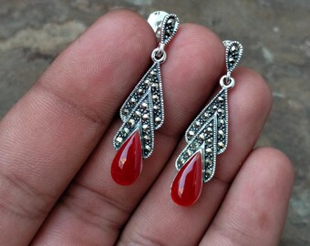 May include: A pair of silver dangle earrings with red gemstone drops. The earrings feature a delicate, intricate design with a marquise-shaped gemstone.