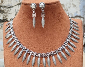 Peut inclure: Un ensemble de collier et boucles d'oreilles en argent avec un motif de feuilles. Le collier a une chaîne avec de petites perles rondes et des pendentifs en forme de feuilles. Les boucles d'oreilles sont de simples clous avec une petite perle ronde et une feuille pendante.