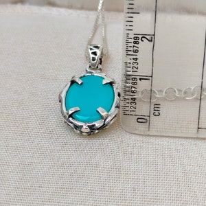 May include: A silver pendant necklace with a turquoise oval stone set in a silver filigree design. The pendant is approximately 1.5 inches long and is hanging from a silver chain.