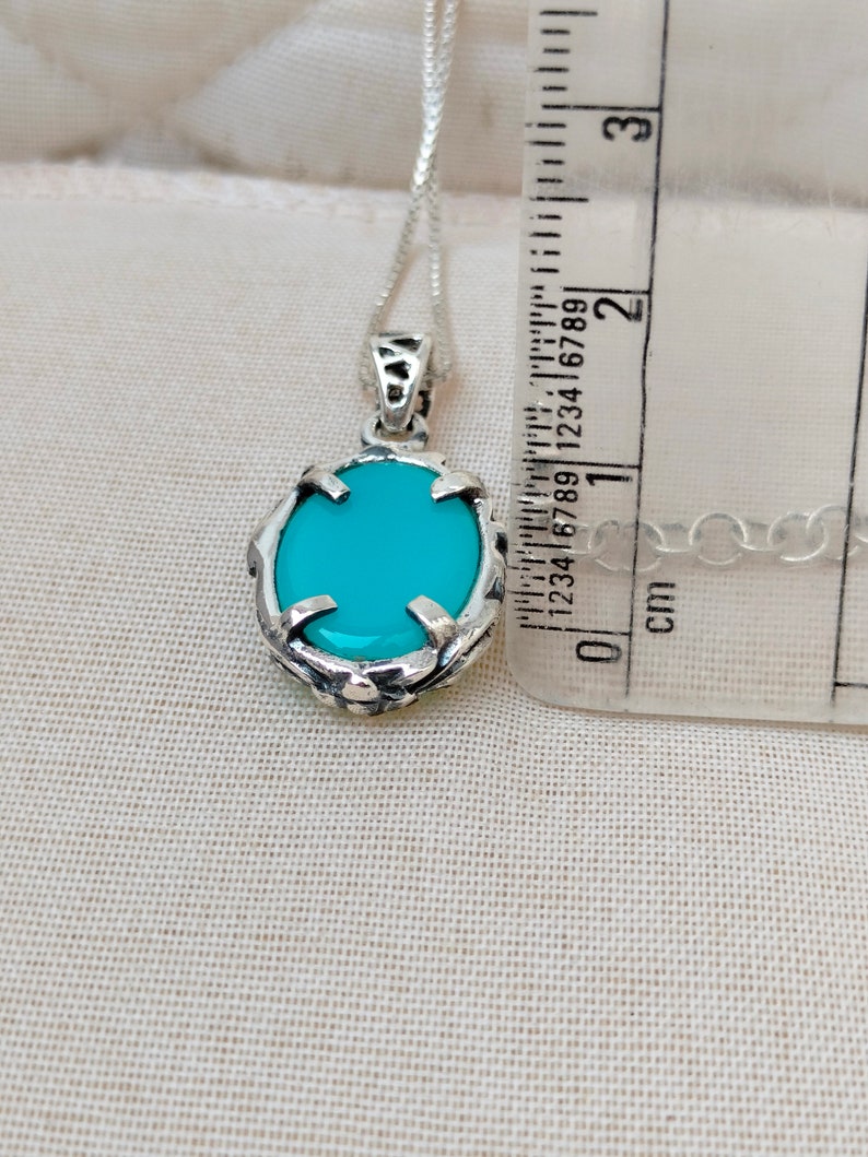 May include: A silver pendant necklace with a turquoise oval stone set in a silver filigree design. The pendant is approximately 1.5 inches long and is hanging from a silver chain.