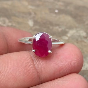Könnte beinhalten: Ein Silberring mit einem großen, oval geschliffenen Rubin. Der Rubin hat eine tiefe, lebendige rote Farbe und wird von vier Krappen gehalten. Der Ring ist dünn und aus glänzendem Silbermetall gefertigt.
