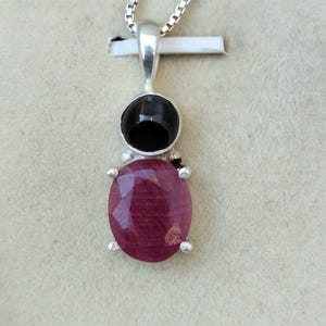 May include: A silver pendant necklace with a red ruby gemstone and a black onyx gemstone.