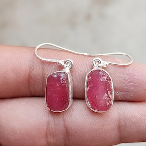 May include: A pair of silver earrings with pink gemstone drops. The earrings have a simple design with a small loop at the top and a rectangular gemstone hanging from it.