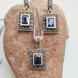 Peut inclure: Un ensemble de collier et boucles d'oreilles en argent avec une pierre pr&eacute;cieuse bleue et des accents de marcassite. Le pendentif et les boucles d'oreilles sont de forme carr&eacute;e avec une pierre pr&eacute;cieuse bleue rectangulaire au centre.