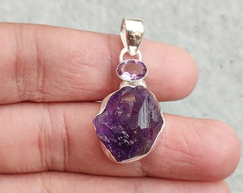 May include: A silver pendant featuring a large, raw amethyst gemstone with a smaller amethyst accent stone. The pendant has a polished silver bail.