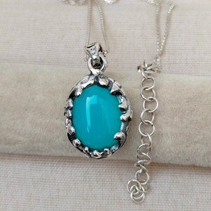 May include: A silver chain necklace with a pendant featuring a turquoise blue oval gemstone set in a silver ornate frame.