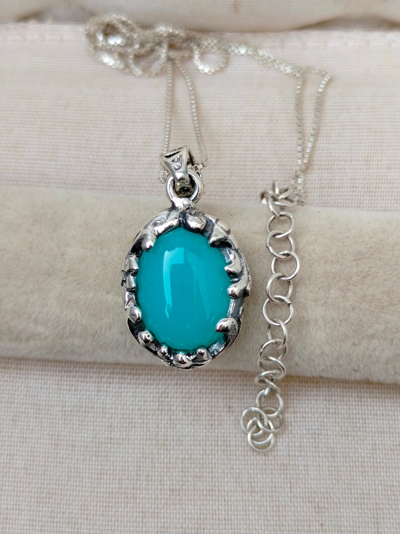 May include: A silver chain necklace with a pendant featuring a turquoise blue oval gemstone set in a silver ornate frame.
