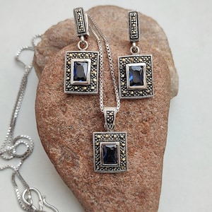Peut inclure: Un ensemble de collier et boucles d'oreilles en argent avec une pierre pr&eacute;cieuse bleue et des accents de marcassite. Le pendentif et les boucles d'oreilles sont de forme carr&eacute;e avec un sertissage &agrave; b&eacute;li&egrave;re.