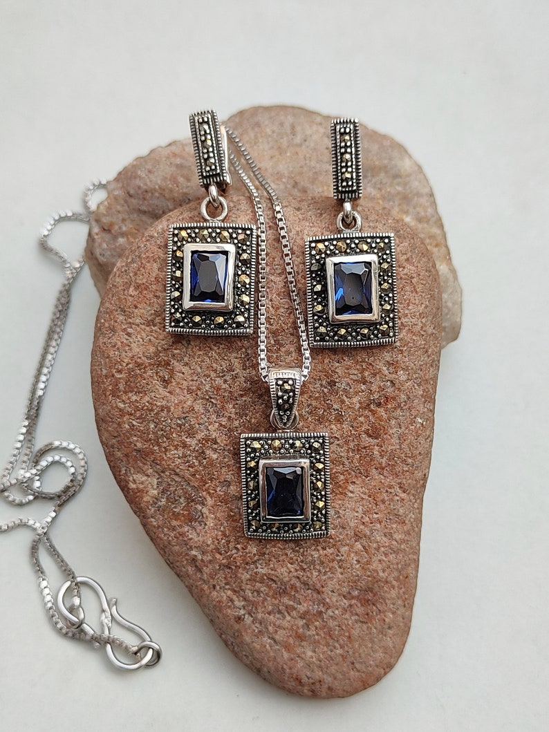 Peut inclure: Un ensemble de collier et boucles d'oreilles en argent avec une pierre pr&eacute;cieuse bleue et des accents de marcassite. Le pendentif et les boucles d'oreilles sont de forme carr&eacute;e avec un sertissage &agrave; b&eacute;li&egrave;re.