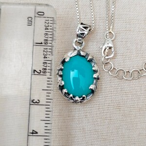 May include: A silver chain necklace with a pendant featuring a turquoise oval gemstone set in a silver filigree frame.