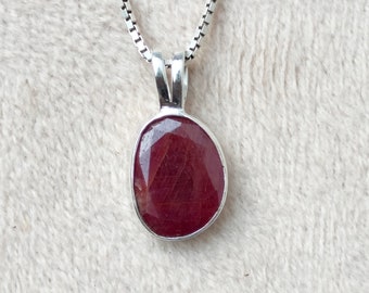 Op de afbeelding: Een zilveren ketting met een hanger met een rode ovale edelsteen.